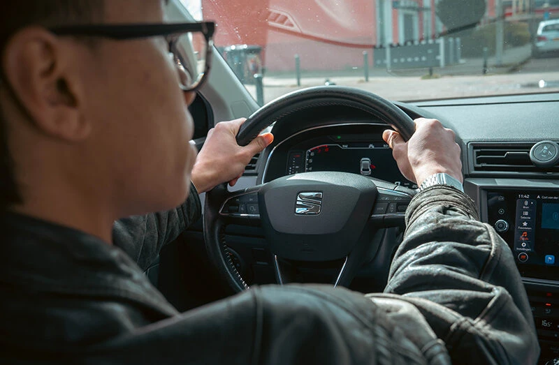 Leerling achter het stuur tijdens een rijles bij Rijschool Caland in Amsterdam, met beide handen aan het stuur en focus op de weg voor een veilige en zelfverzekerde rijervaring.